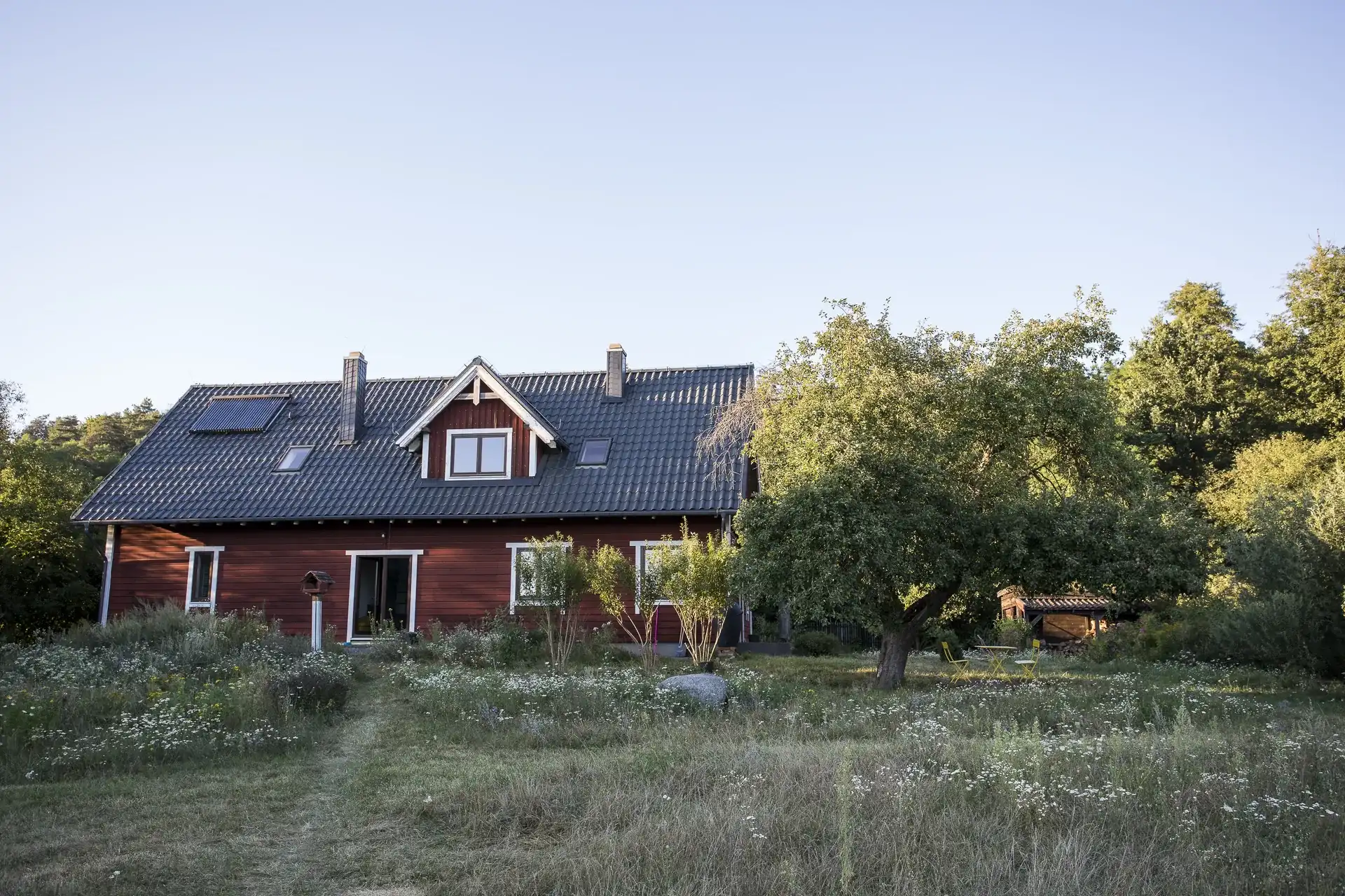 Czerwony drewniany dom z apartamentem, widziany od strony łąki w Drwałach